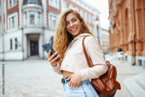 Young woman messaging on phone outside. Beautiful woman smiles sincerely and walks outdoors. Fashion style.