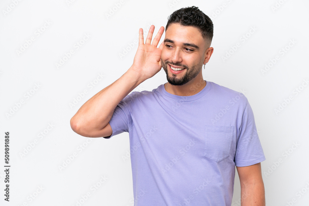 Fototapeta premium Young Arab handsome man isolated on white background listening to something by putting hand on the ear