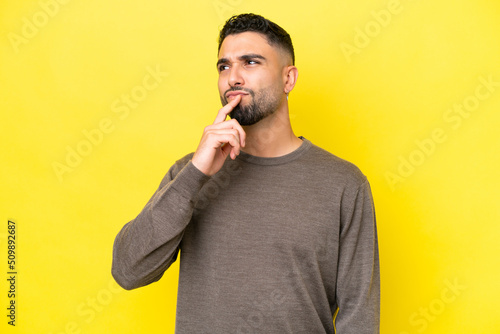 Young Arab handsome man isolated on yellow background having doubts while looking up