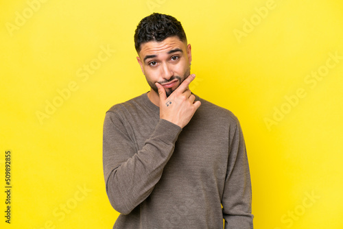 Young Arab handsome man isolated on yellow background having doubts