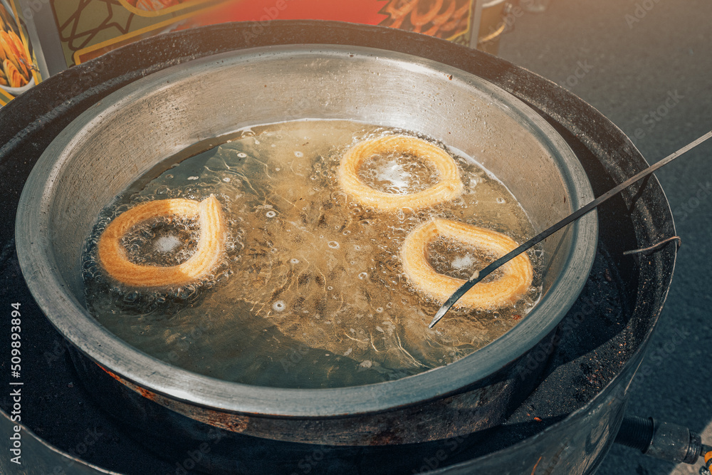 Spanish churros are boiled in boiling oil in a street food cafe