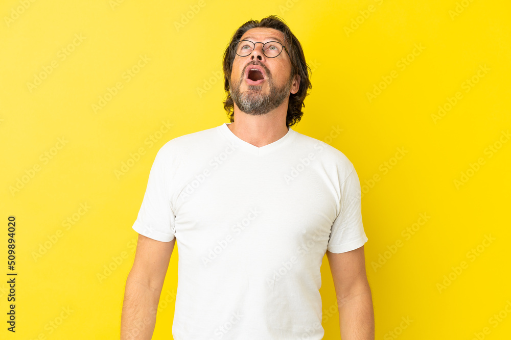 Senior dutch man isolated on yellow background looking up and with surprised expression Senior dutch man isolated on yellow background looking up and with surprised expression