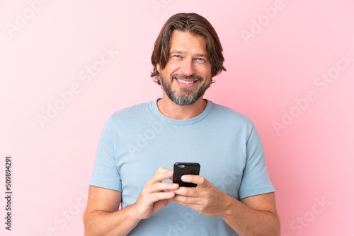 Senior dutch man isolated on pink background looking at the camera and smiling while using the mobile © luismolinero