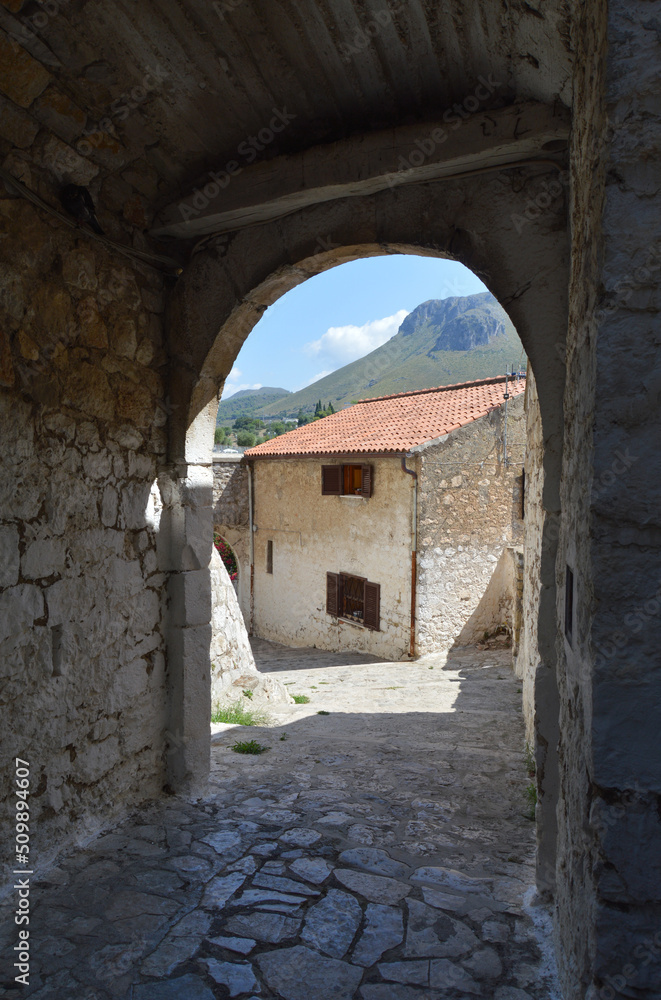 View of stone building and mountains through dark alleyway in Sperlonga, Italy