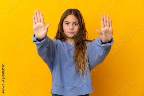Child over isolated yellow background making stop gesture and disappointed