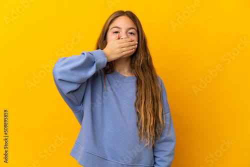 Child over isolated yellow background covering mouth with hand © luismolinero
