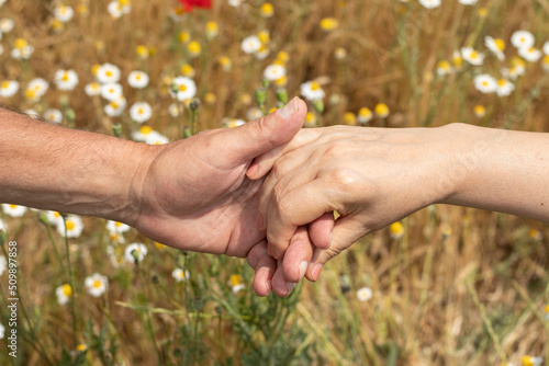 A close-up of two adult hands holding each other on a sunny day in nature. Christian middle-aged couple love, care, compassion concept. Help and support gesture. A closeup. © Marinela
