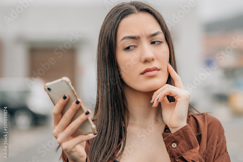 Vászonkép girl looking at the mobile phone pensive with mistrust