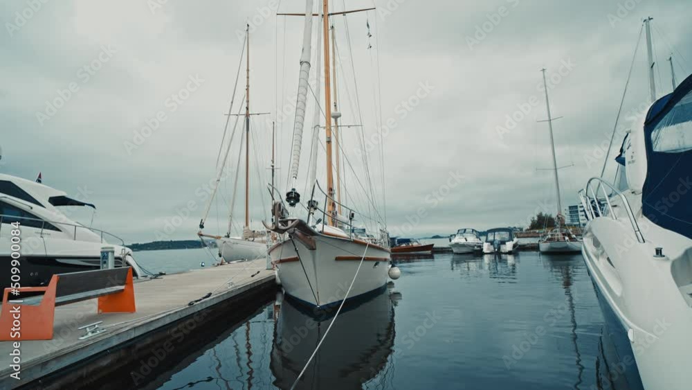 Blue sailboat moored to a pier in yacht marina at sunset. Colorful cloudscape, reflections on the water. Sailing, recreation theme. Blue sailboat moored to a pier in yacht marina at sunset. Colorful cloudscape, reflections on the water. Sailing, recreation theme.