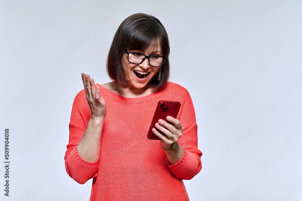 Naklejka premium Middle aged smiling woman looking into smartphone on light studio background