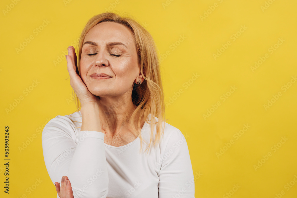 Naklejka premium Portrait of mature beautiful woman holding hand near face on yellow background