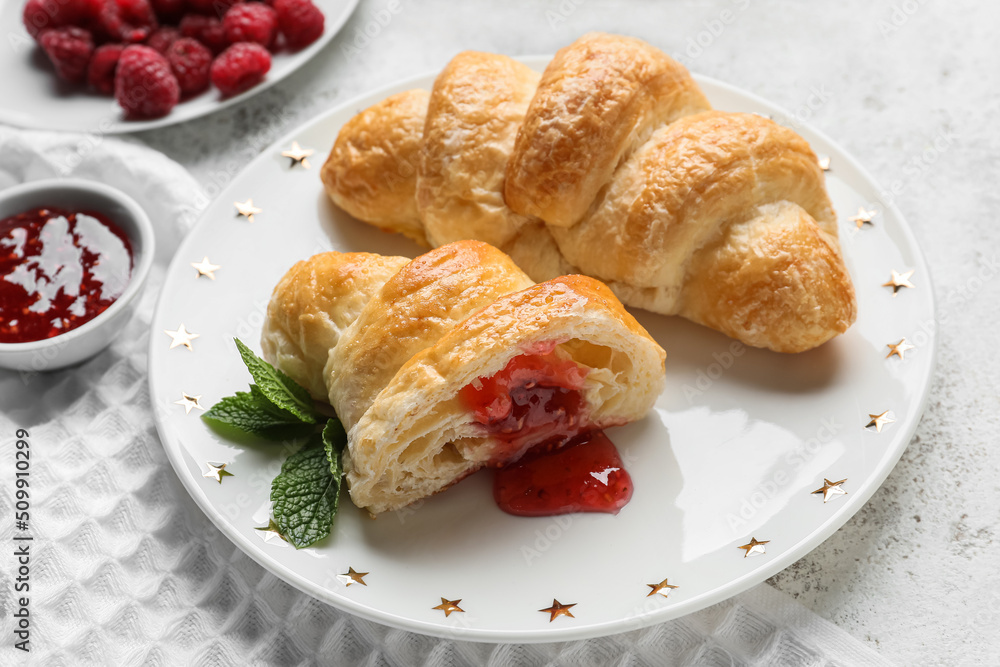 Plate of delicious croissants with raspberry jam on light background