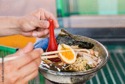 Mano sosteniendo huevo y cuchara de ramen 