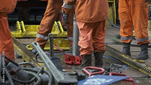 Drilling platform. Rotor table. Manual slips is being installed. Legs in orange coveralls. Drill floor. RIG.