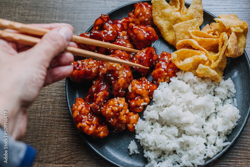 General Tsos Chicken with white rice and crab rangoon on a dark dish photo