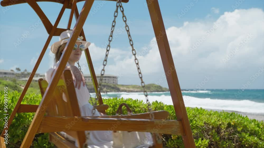 Young smiling woman swinging on wooden swing in luxury beach resort park with scenic ocean views. Happy summer vacation dream concept. Elegant lady on wooden swing enjoying holidays on Hawaii, RED 4K Young smiling woman swinging on wooden swing in luxury beach resort park with scenic ocean views. Happy summer vacation dream concept. Elegant lady on wooden swing enjoying holidays on Hawaii, RED 4K