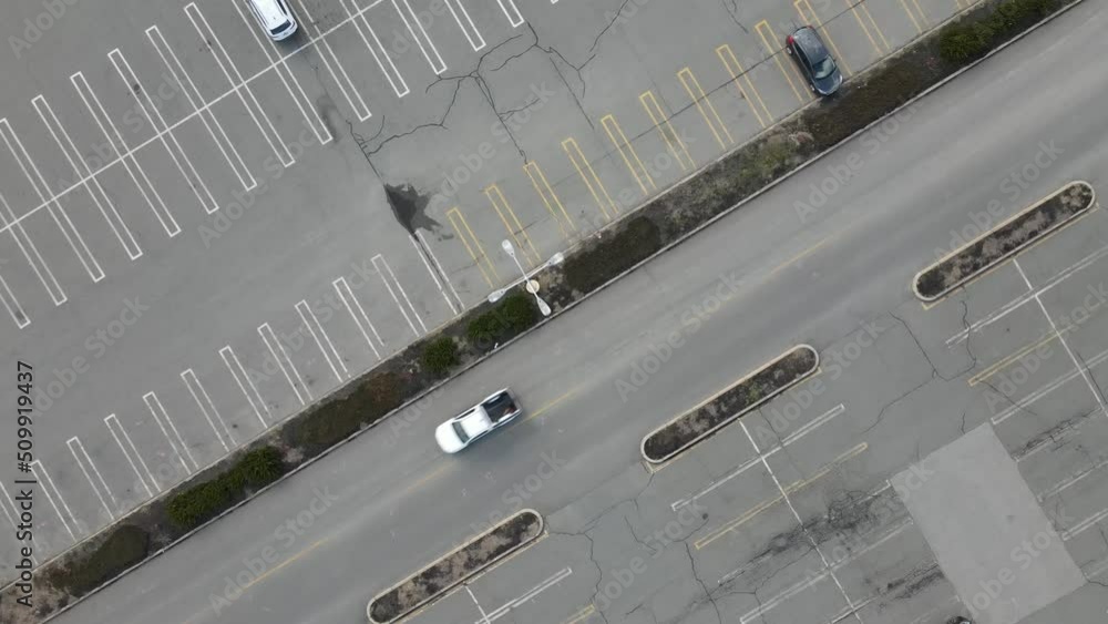 Static birds eye view of a parking lot and mall access road with traffic passing and lot light poles visible. Static birds eye view of a parking lot and mall access road with traffic passing and lot light poles visible.