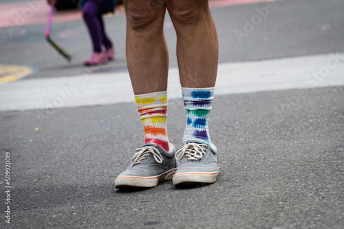 A photo of old blue shoes with colorful orange, yellow and blue socks on an outdoor street during a gay pride parade.