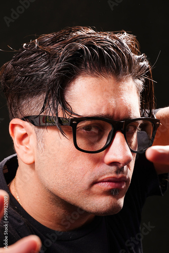 Tableau sur toile close-up of man with defiant look, looking at camera, wearing black glasses, black t-shirt on black background