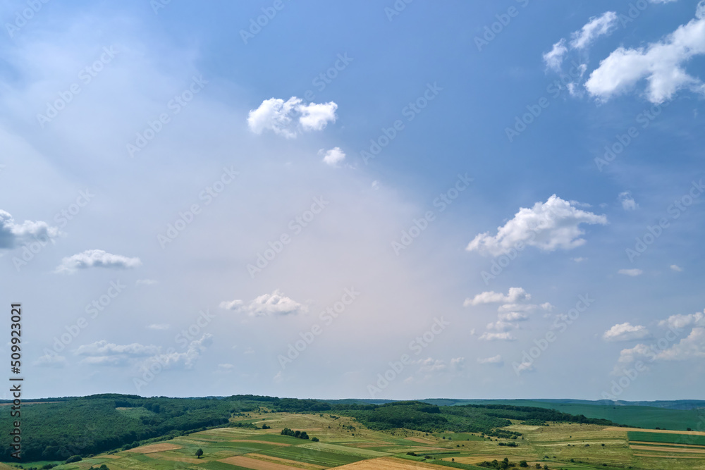 Aerial landscape view of clear blue sky over green cultivated agricultural fields with growing crops and distant woodland on bright summer day Aerial landscape view of clear blue sky over green cultivated agricultural fields with growing crops and distant woodland on bright summer day