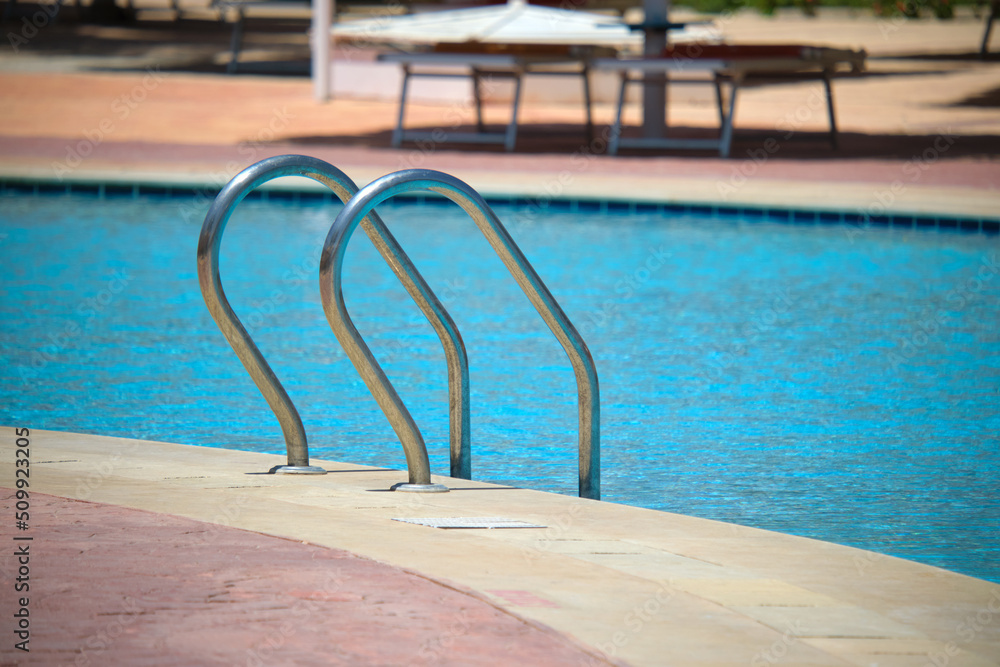 Close up of swimming pool stainless steel handrail descending into tortoise clear pool water. Accessibility of recreational activities concept