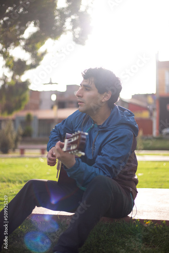 joven cantando y tocando guitarra en un parque al atardecer. Concepto de personas y musica.