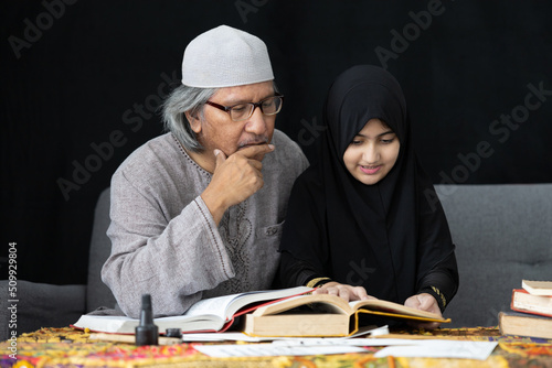 muslim father teaching his daughter about practicing reading textbook on black background