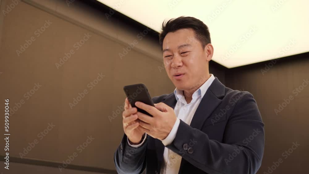 Portrait of happy lucky asian businessman enjoy success on mobile phone at office. Closeup overjoyed chinese man reading good news on phone raises hand up. Surprised male celebrating victory on phone. Portrait of happy lucky asian businessman enjoy success on mobile phone at office. Closeup overjoyed chinese man reading good news on phone raises hand up. Surprised male celebrating victory on phone.