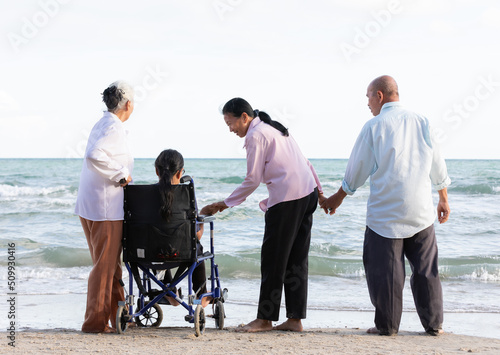 back view senior woman in a wheelchair with friends enjoy travel on the beach