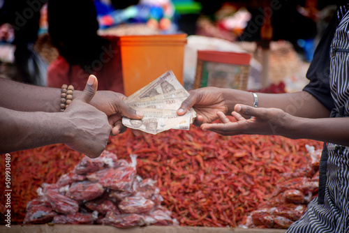 Two African hands of a seller and buyer exchanging money, cash, currency or naira notes in a market place during transaction