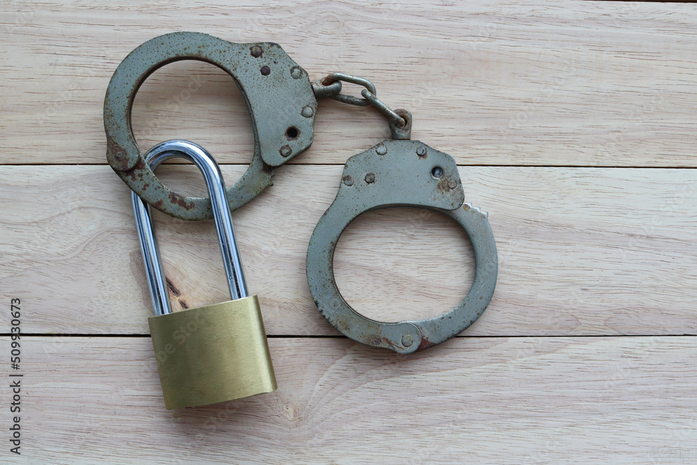 Metal padlock with steel police handcuff isolated on wooden background closeup. Metal padlock with steel police handcuff isolated on wooden background closeup.