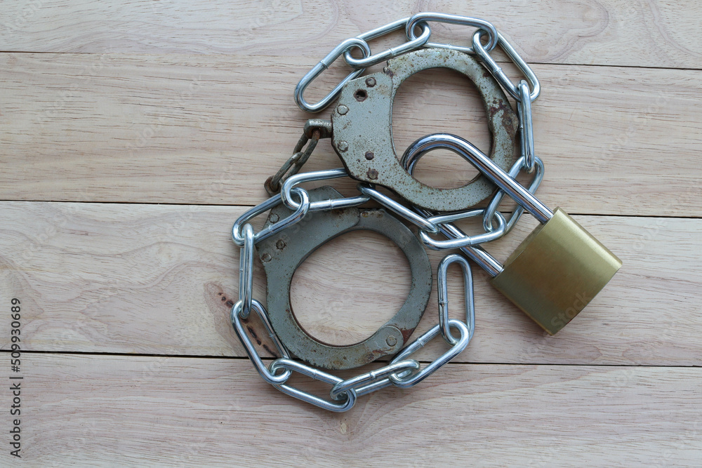Obraz premium Metal padlock and steel chain with rusty handcuffs isolated on wooden background closeup.