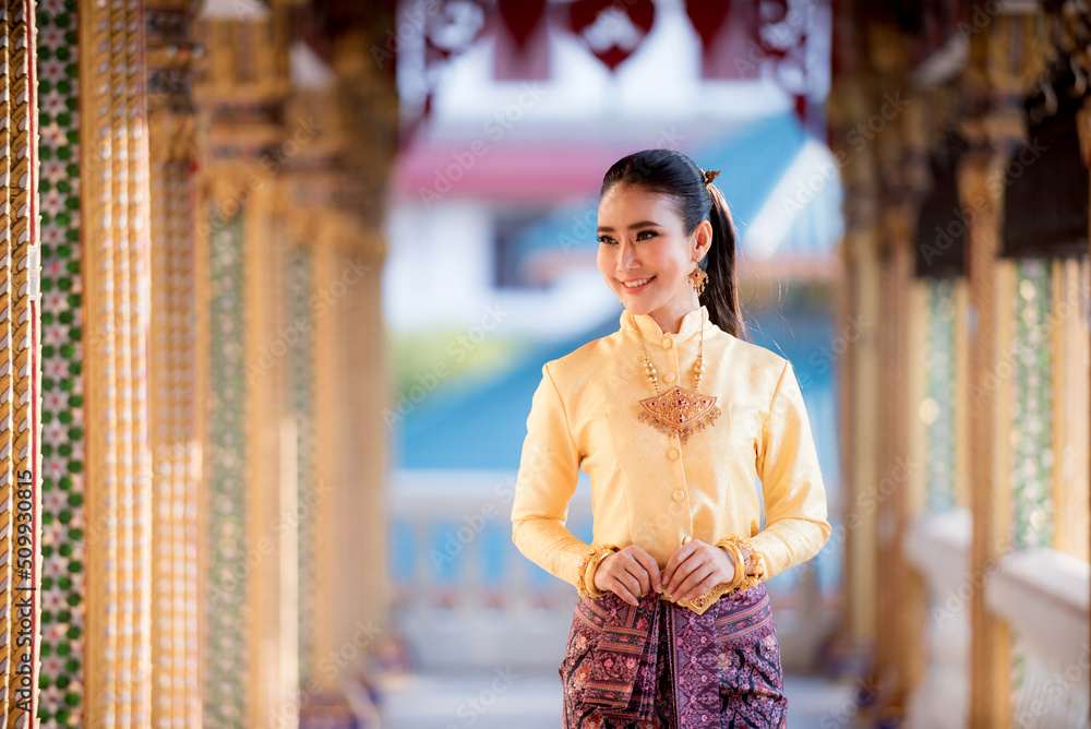 Fototapeta premium Portrait of a beautiful woman wearing a traditional Thai dress smiling gracefully standing in a temple of Thailand