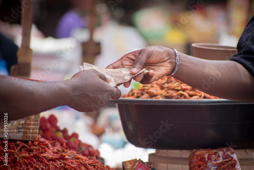 Two African hands of a seller and buyer exchanging money, cash, currency or naira notes in a market place during transaction