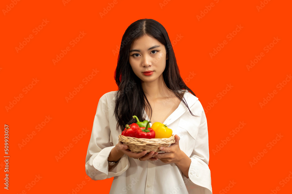 Vegetarian concept, Healthy woman hold basket of colorful bell pepper isolated on orange background Vegetarian concept, Healthy woman hold basket of colorful bell pepper isolated on orange background