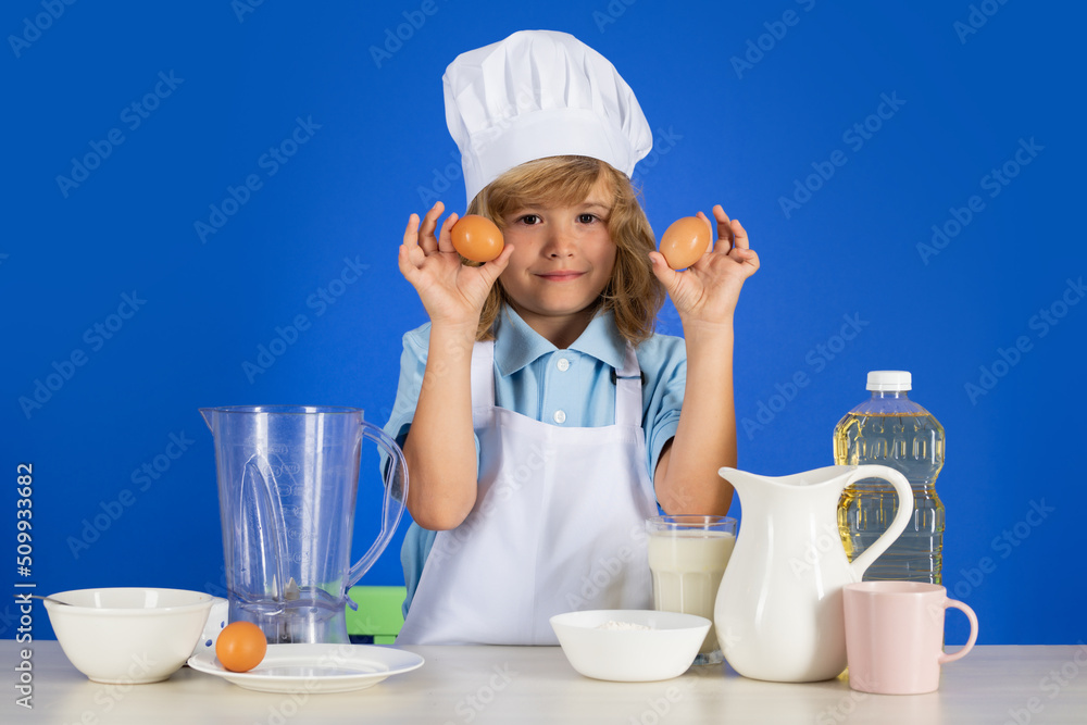 Cooking children. Chef kid boy hold eggs making fresh vegetables for healthy eat. Portrait of little child in form of cook isolated on grey background. Kid chef. Cooking process. Cooking children. Chef kid boy hold eggs making fresh vegetables for healthy eat. Portrait of little child in form of cook isolated on grey background. Kid chef. Cooking process.
