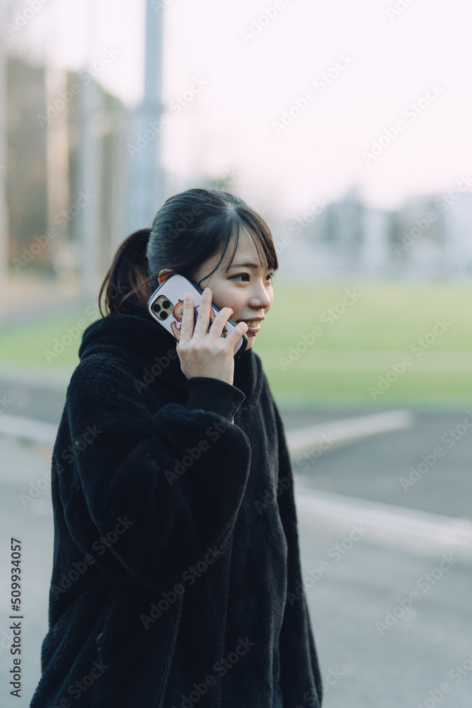 愛知県名古屋市の鶴舞公園をスマートフォンで通話をしている若い女性 Young woman talking on her smartphone in Tsurumai Park, Nagoya, Aichi, Japan. 