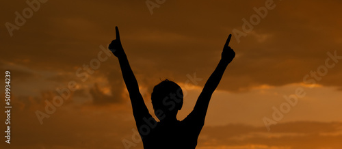 Panoramic Silhouette of a kid raising his arms and doing peace sign with his hand in front of the beautiful sunset