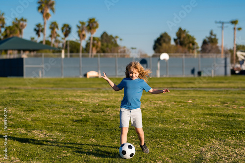 Young soccer player in sportswear with soccer ball. Cheerful little boy enjoy soccer, football sport games. Kid kicking a football ball on a grass.