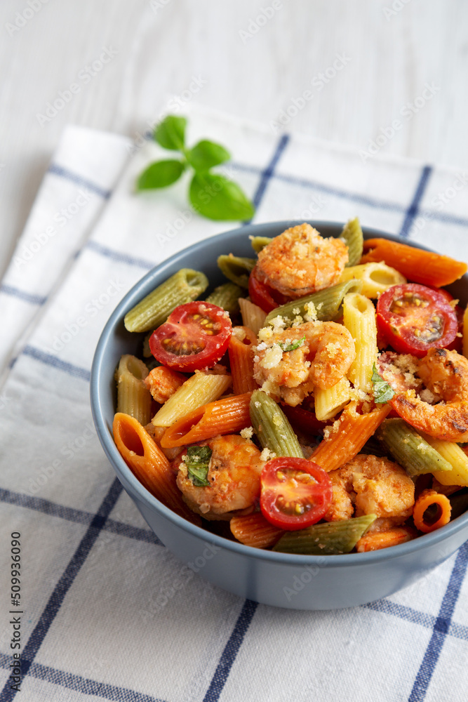 Homemade Tri-Color Penne Salad with Shrimp, Tomato and Basil Bread Crumbs in a Bowl on a white wooden background, side view. Homemade Tri-Color Penne Salad with Shrimp, Tomato and Basil Bread Crumbs in a Bowl on a white wooden background, side view.