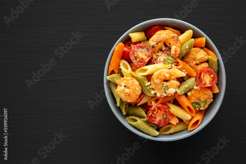 Homemade Tri-Color Penne Salad with Shrimp, Tomato and Basil Bread Crumbs in a Bowl on a black background, top view. Flat lay, overhead, from above. Copy space.