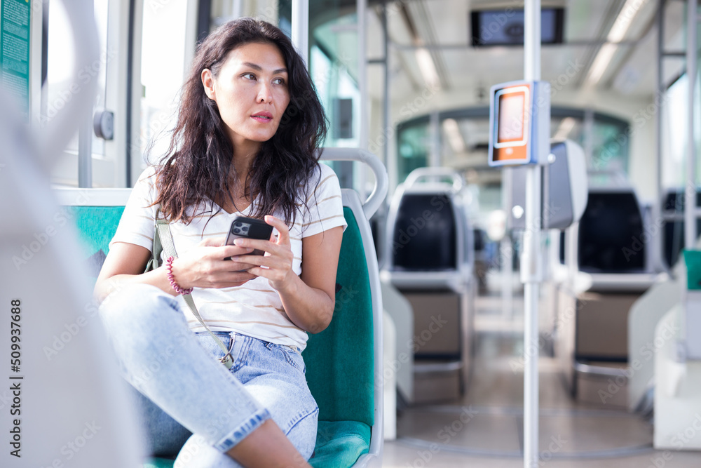 Oriental woman sitting inside tram with smartphone in hand.