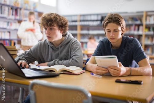 Two teenage friends are reading books and preparing for exams in the school library