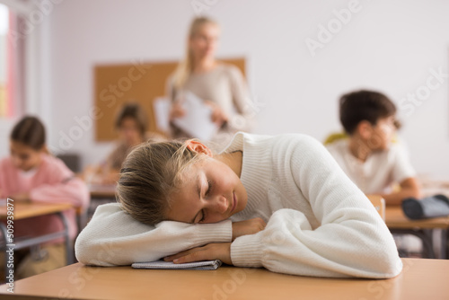 Tired bored teenage schoolgirl sleeping at desk