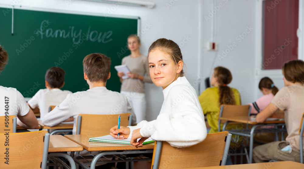 Fototapeta premium Teenage girl turned around and looking at camera during lesson in classroom.