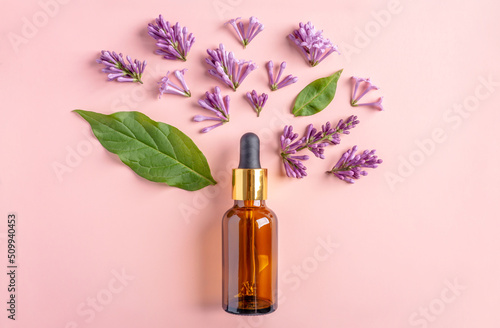 Glass bottle with cosmetic oil and leaves and flowers lilac on a pink background