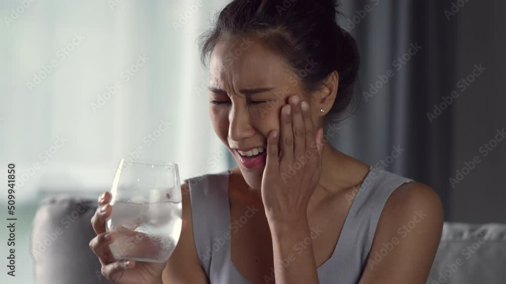 Young Asian woman have toothache while drinking water with ice from glass. Health care concept. Young Asian woman have toothache while drinking water with ice from glass. Health care concept.