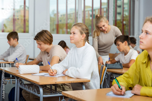 Group of diligent school kids and teacher during lesson in classroom in secondary school