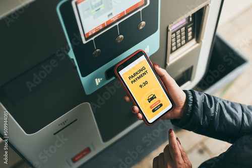 Woman paying for parking ticket at car parking payment machine using mobile app on smartphone. Car parking application on mobile phone