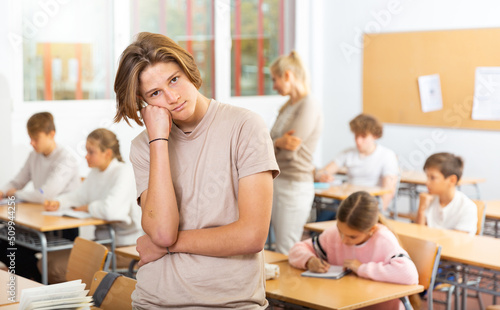 Portrait of thoughtful teenager boy standing in classroom during lesson in school.